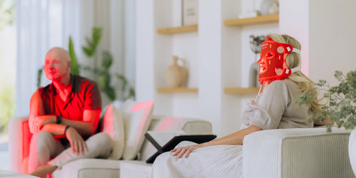 Twee personen op de bank, waarvan een het Liroma LED masker voor rood licht therapie draagt