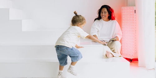 Vrouw met kind in de woonkamer naast een Liroma Elite roodlichttherapie paneel